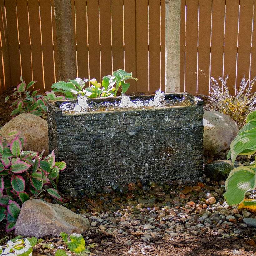 Custom fountain setup using stacked slate wall base and topper with water cascading over textured stone finish.