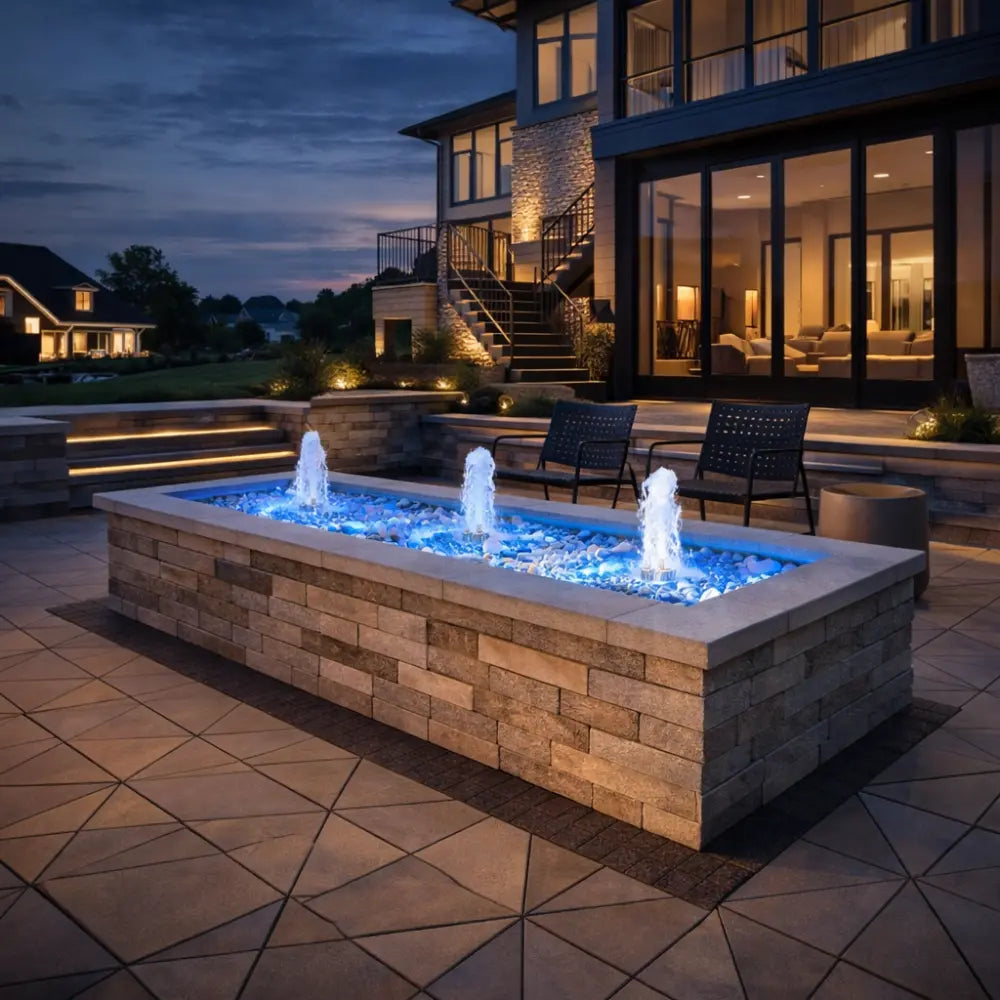 Outdoor stone fire pit with water feature in front of a house at night