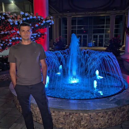 Man standing in front of a blue illuminated fountain at night.