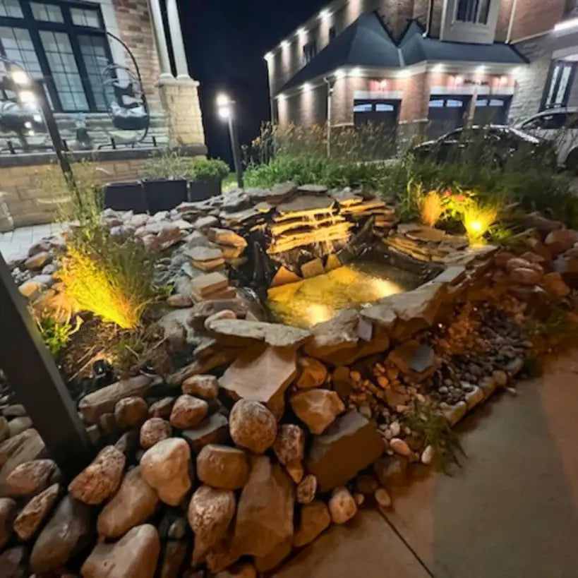 Rock garden with illuminated water feature in front of a building at night
