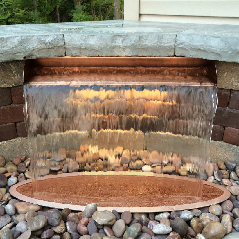 Waterfall feature with transparent glass panel and stone base in outdoor setting