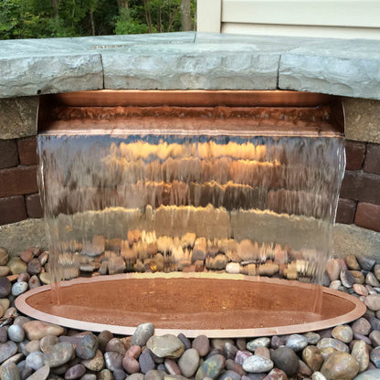 Waterfall feature with transparent glass panel and stone base in outdoor setting