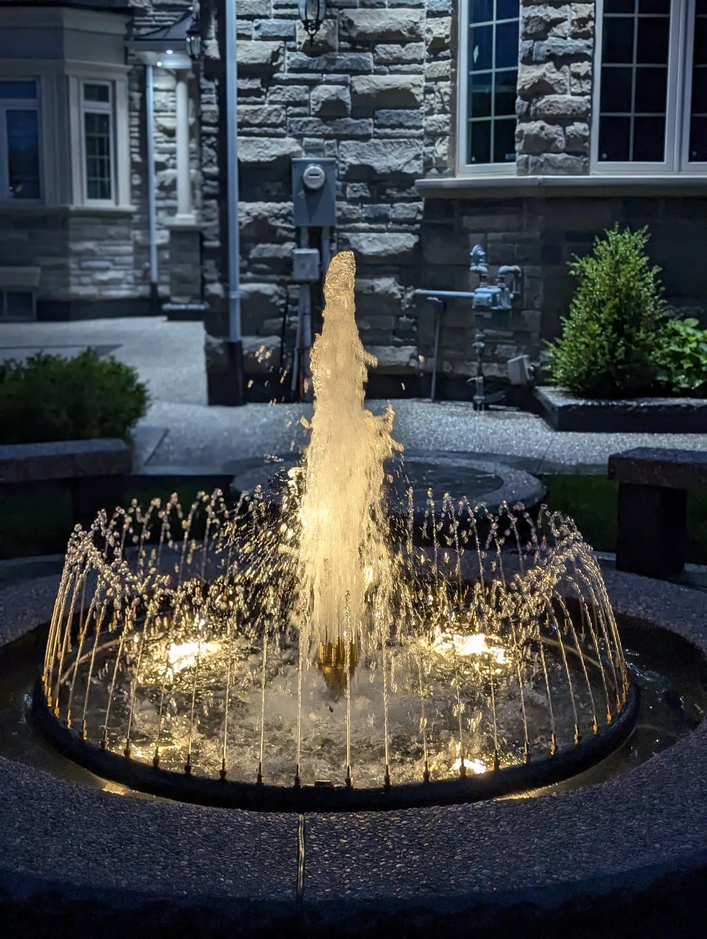 Spray Ring fountain with center column jet with Aquascape lighting at night built by AquaGarden